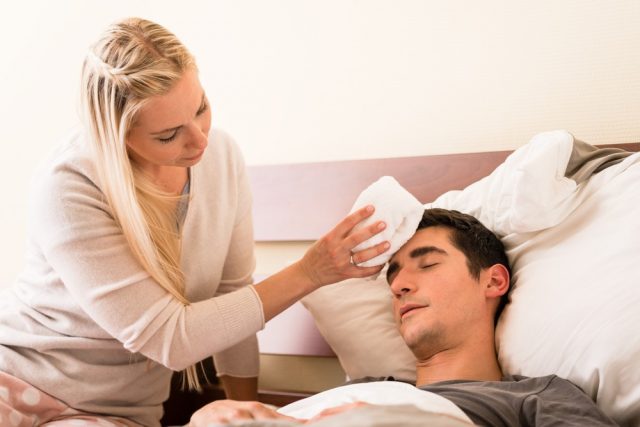 Young caring woman holding a cold compress on the forehead of her sick partner