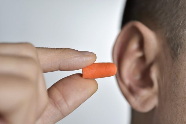young man inserting an orange earplug in his ear