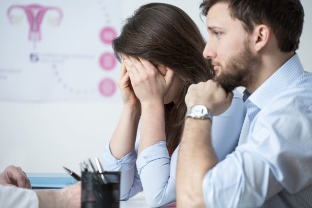 Crying young woman sitting with husband at gynecologist office