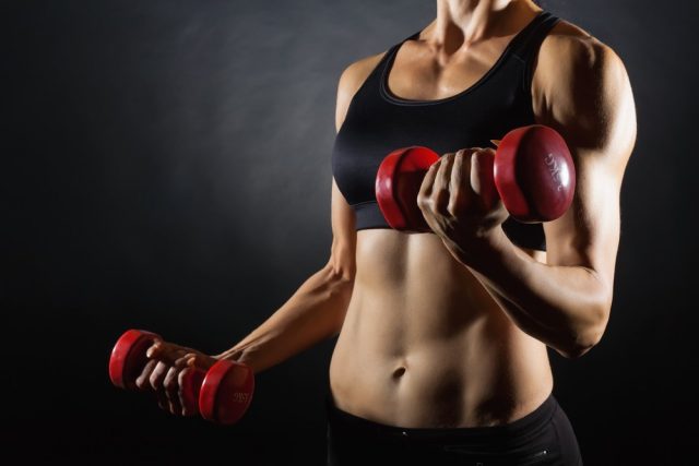 Torso of a young fit woman lifting dumbbells