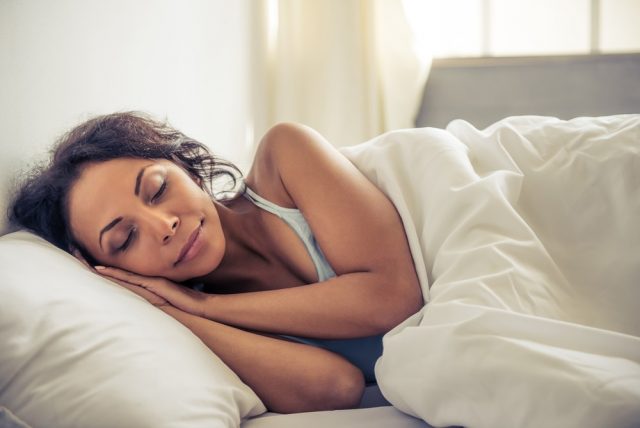 Side view of beautiful young Afro American woman smiling while sleeping in her bed at home