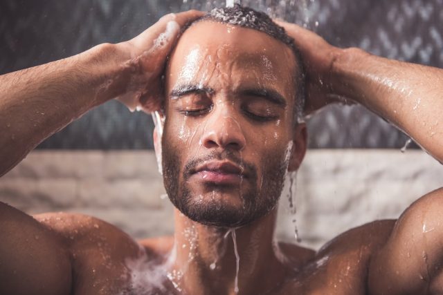 Handsome naked Afro American man is taking shower in bathroom