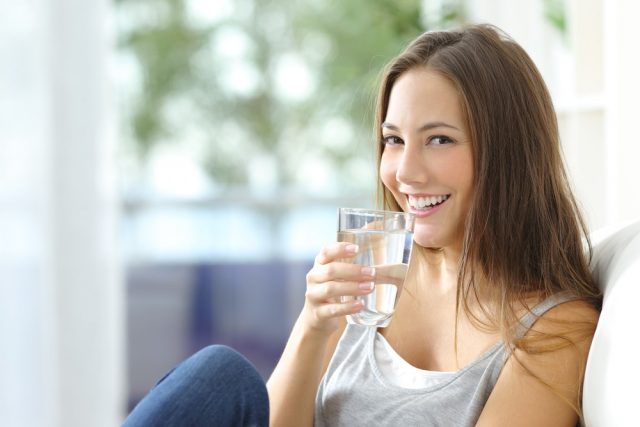 Girl drinking water sitting on a couch at home