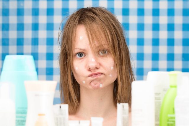 Young white-skinned girl with wet hair without makeup is in disbelief in front of cosmetic products