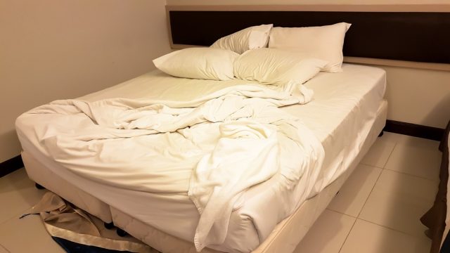 dirty bed with white pillow and white blanket in the room