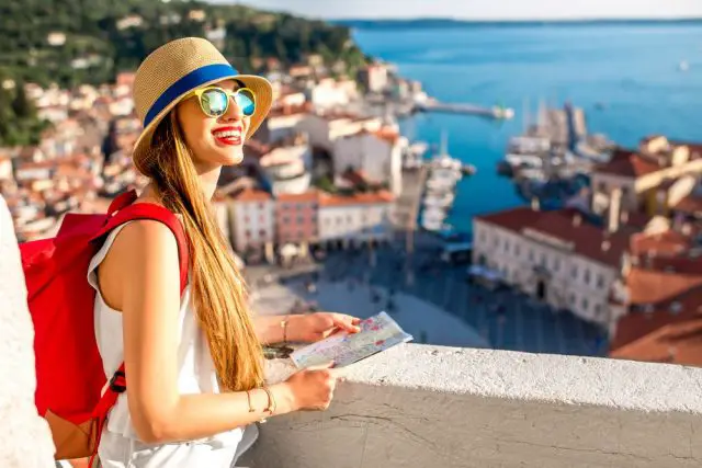 Young female traveler with red backpack and hat enjoying the view from George's tower on Piran old town