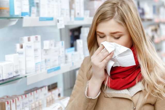 Young woman sneezing in a paper napkin while shopping at the drugstore