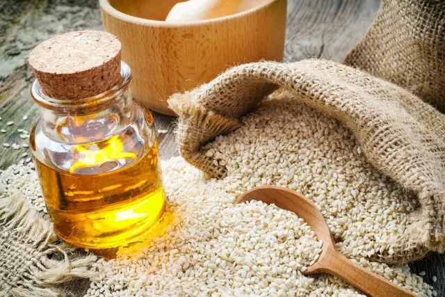 sesame seeds in sack and bottle of sesame oil on wooden rustic table