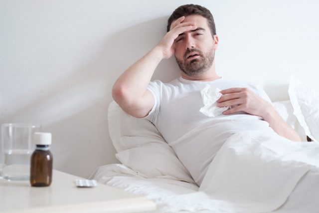 Man feeling cold, lying in the bed and blowing his nose