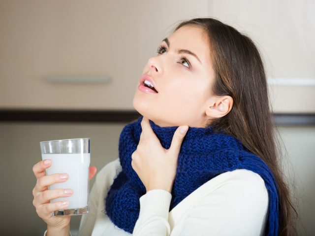 Young brunette in scarf gargling throat with medicine