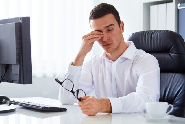 Young tired businessman rubbing his eye