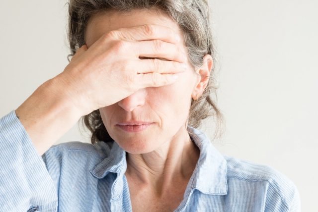 Close up of middle aged woman with hand covering eyes