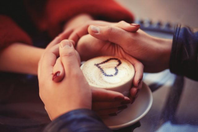 Four hands wrapped around a cup of coffee with heart drawing