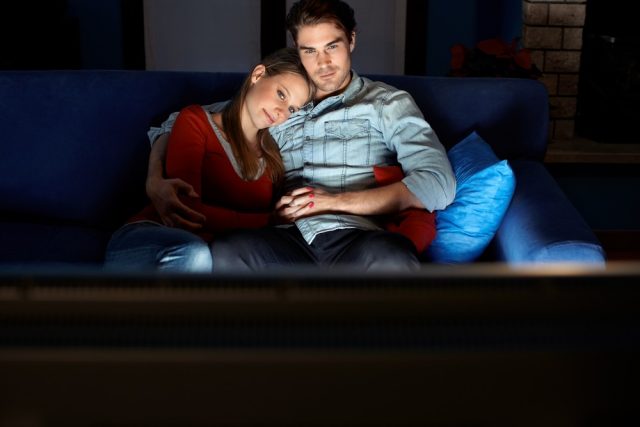 Young heterosexual couple hugging on sofa and watching movie on tv at home