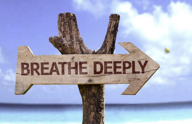 Breathe Deeply wooden sign with a beach on background