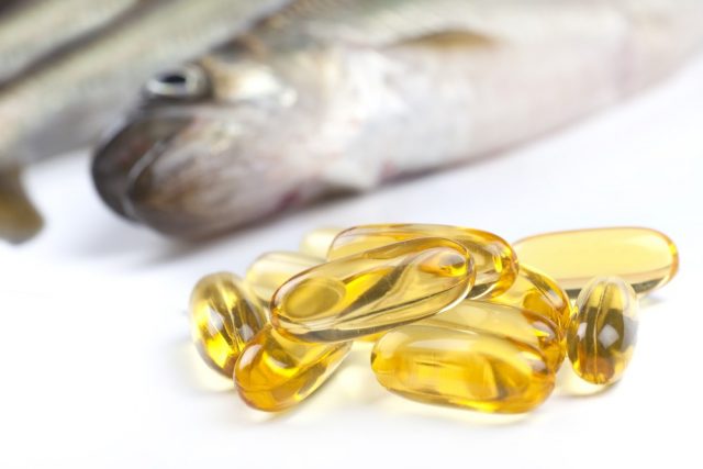 Close up of a cod liver fish oil capsule, a nutritional supplement high in omega-3 fatty acids, EPA, DHA, and high levels of vitamin A and vitamin D. Fresh fish are in the background.