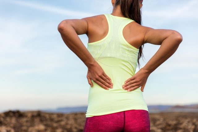 Trail running runner with painful lower back pain injury or strained muscle near the spine