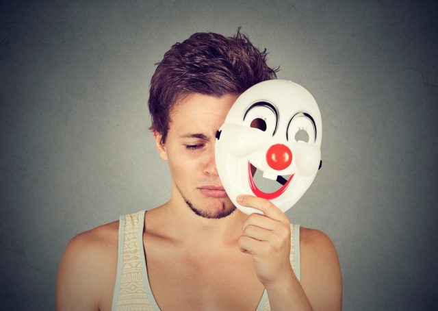 Young sad man taking off clown mask