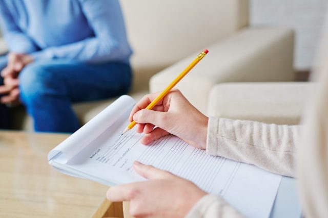 Psychologist in brown cardigan sitting on armchair and making diagnosis to her depressed patient