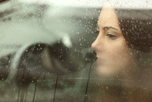 Sad woman or teenager girl looking through a steamy car window